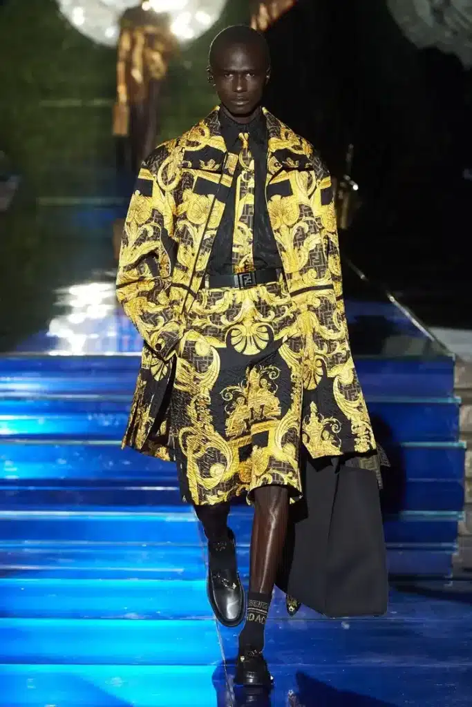 runway image showing a black model for versace wearing an outfit featuring its iconic versace print