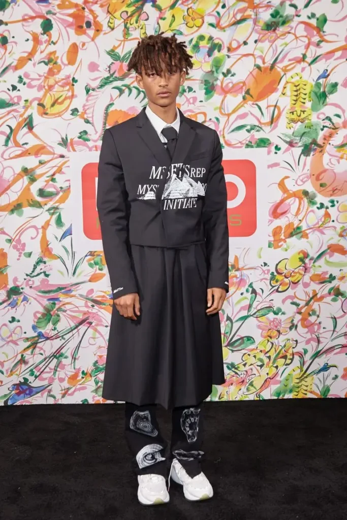 jaden wearing a cropped black suit jacket with a graphic on it and combining it with a long black skirt with black pants under