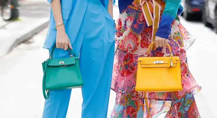 Two women carrying hermes kelly bags, one green and the other yellow.