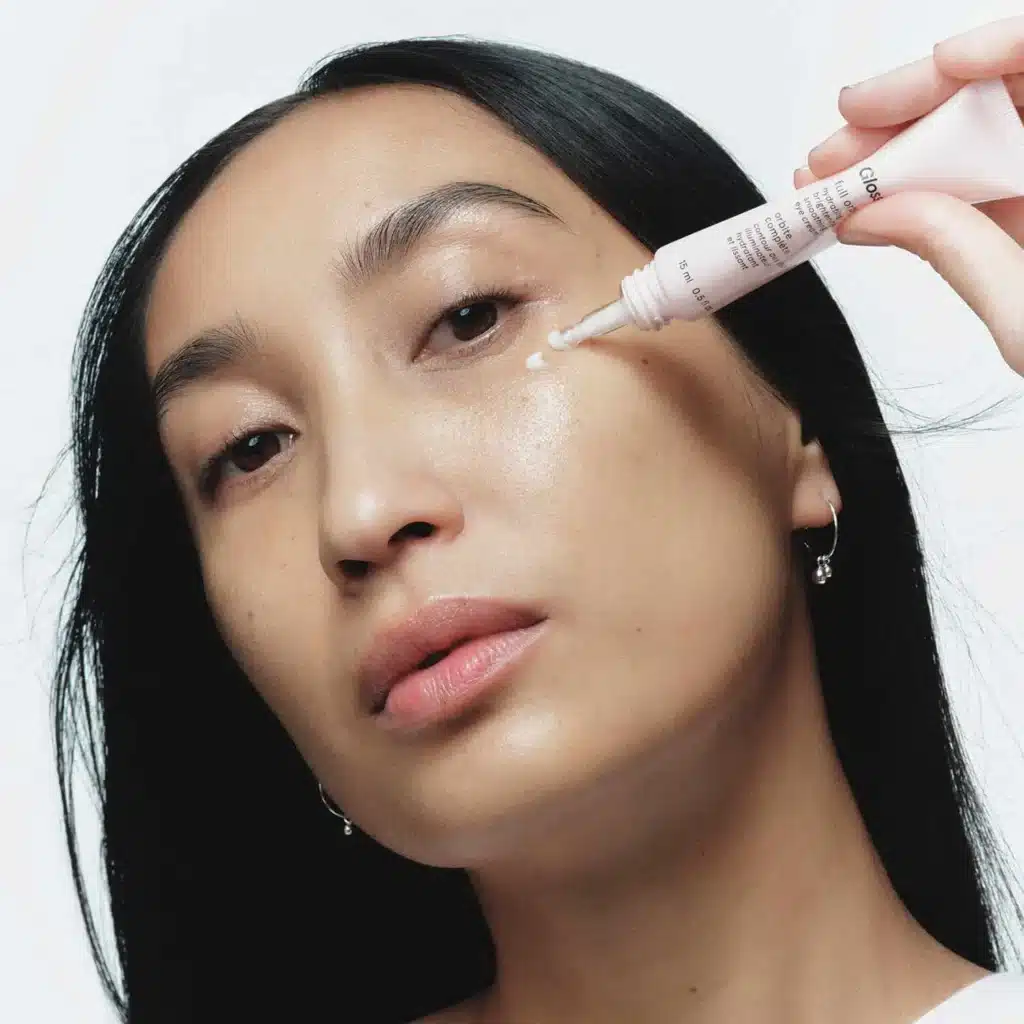 Model applying glossier eye cream on their under eye