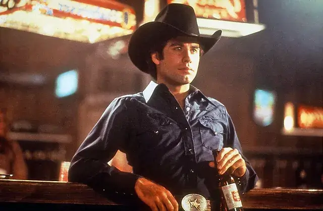 John Travolta in the movie Urban cowboy wearing a cowboy hat, shirt and belt standing at a bar