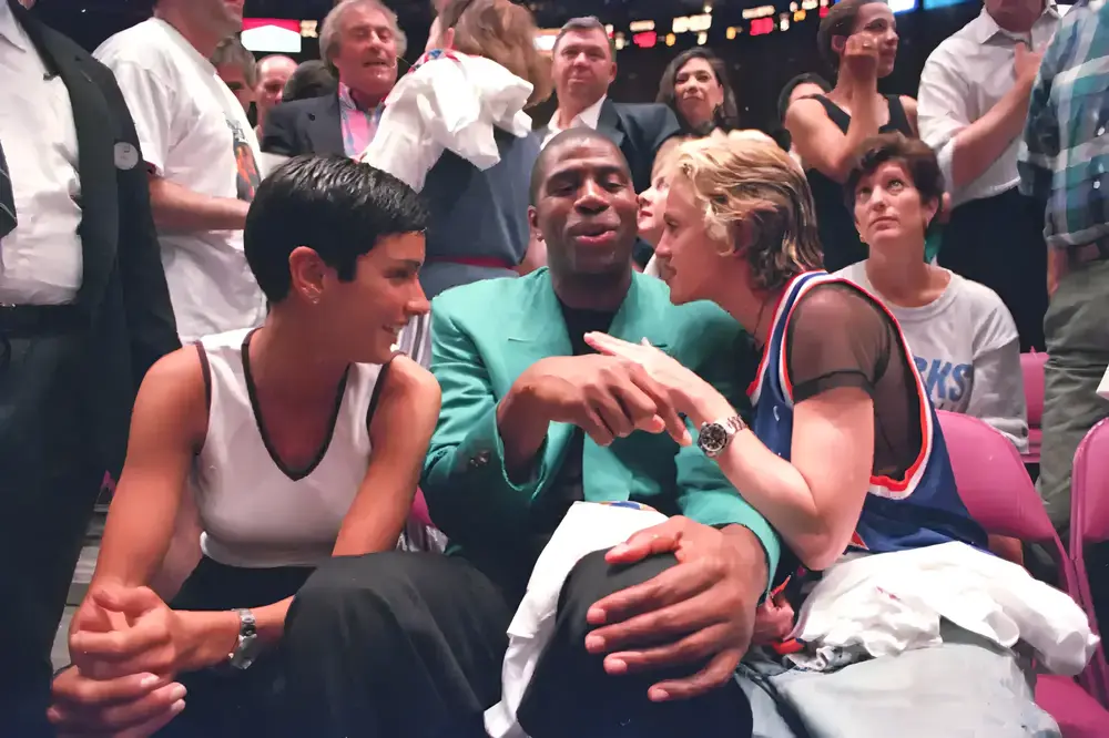 Madonna, Magic Johnson, and Ingrid Casares seated together at the 1994 NBA Finals between the Houston Rockets and the New York Knicks, engaged in conversation with other spectators in the background.