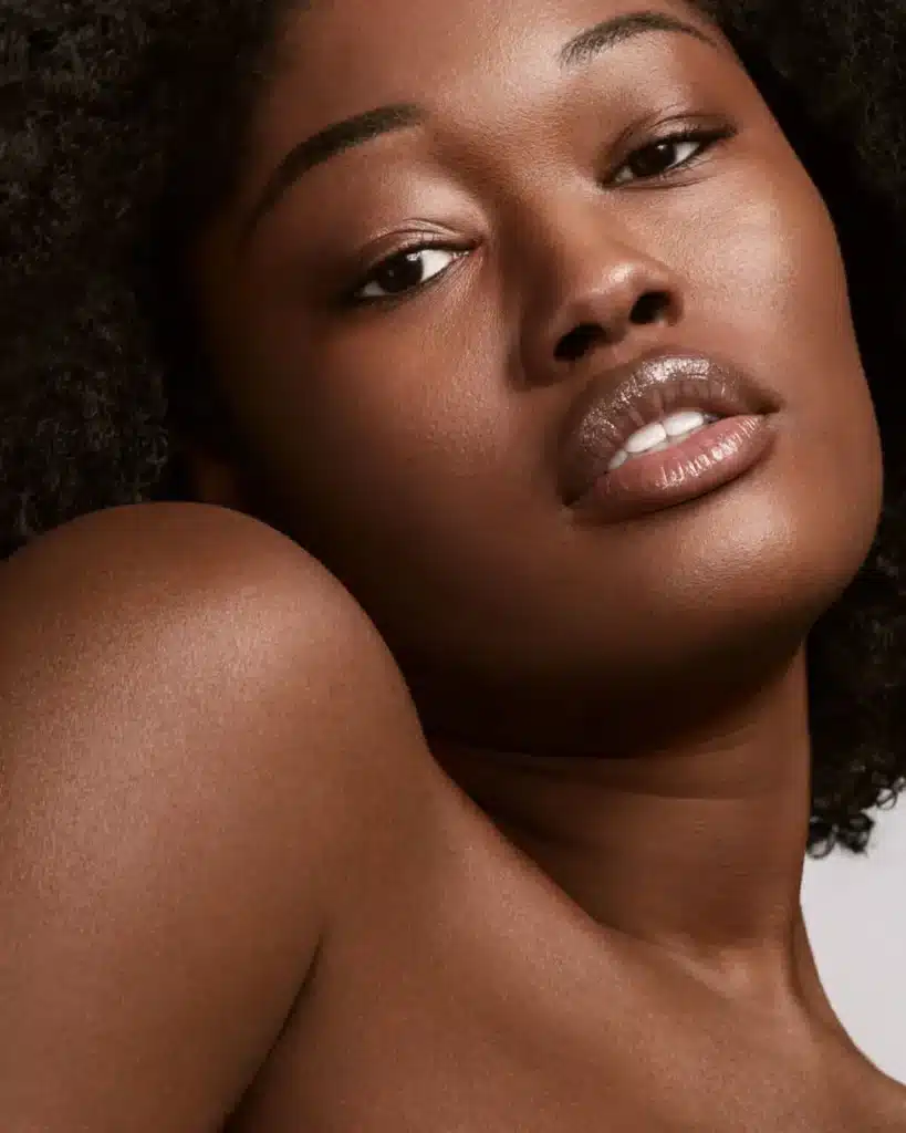 Close-up of a model with deep skin tone and glossy lips wearing Fenty Beauty products.