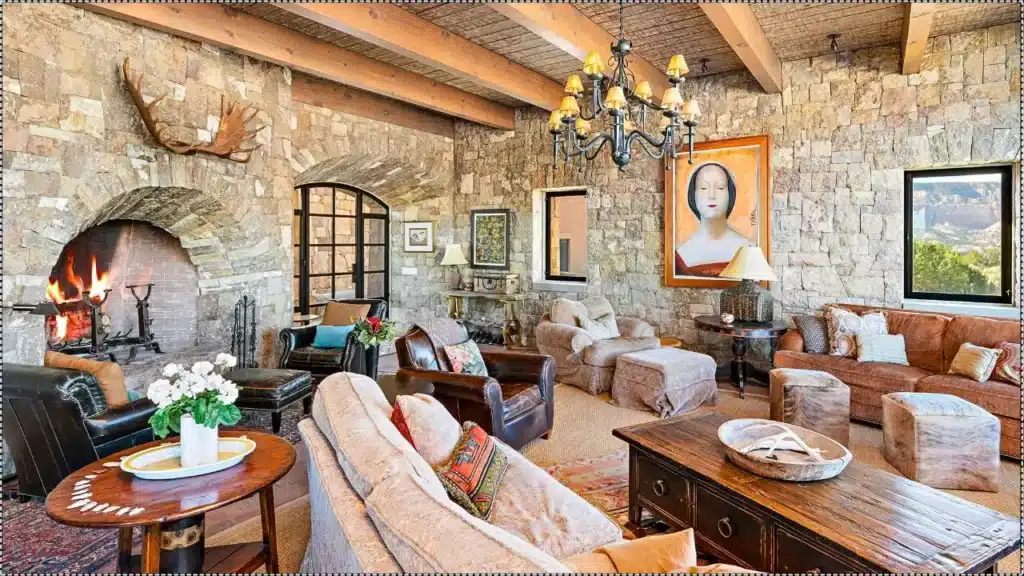 Rustic living room at Tom Ford’s Cerro Pelon Ranch in New Mexico, featuring stone walls and a large fireplace.